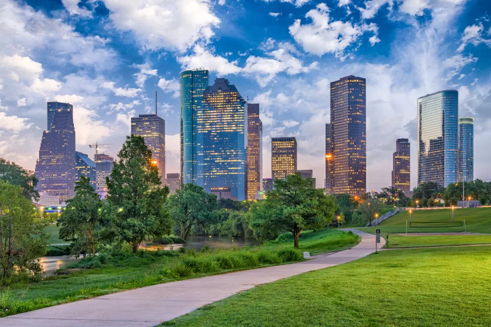 Green lawn and walkway in downtonw Houston park with skyline in background.